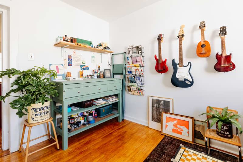 Corner view shows graphic arts work area and guitars hung on wall in white room.