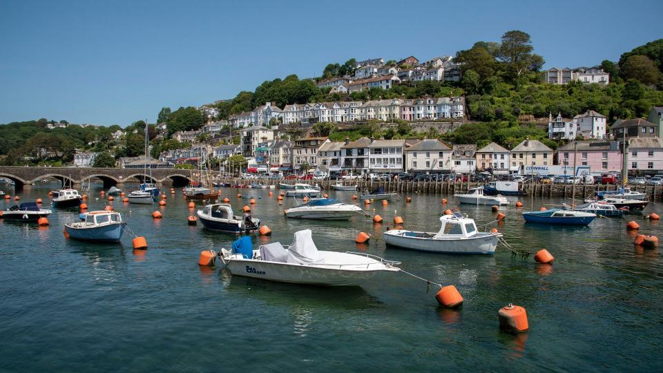 Houses perched on a seafront cliffside and near the water, boats moored in the water in the foreground