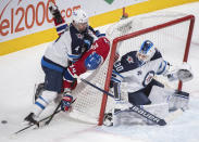 Winnipeg Jets goaltender Laurent Brossoit looks on as Jets' Neal Pionk (4) upends Montreal Canadiens' Corey Perry (94) during the third period of an NHL hockey game Saturday, March 6, 2021, in Montreal. (Graham Hughes/The Canadian Press vIa AP)