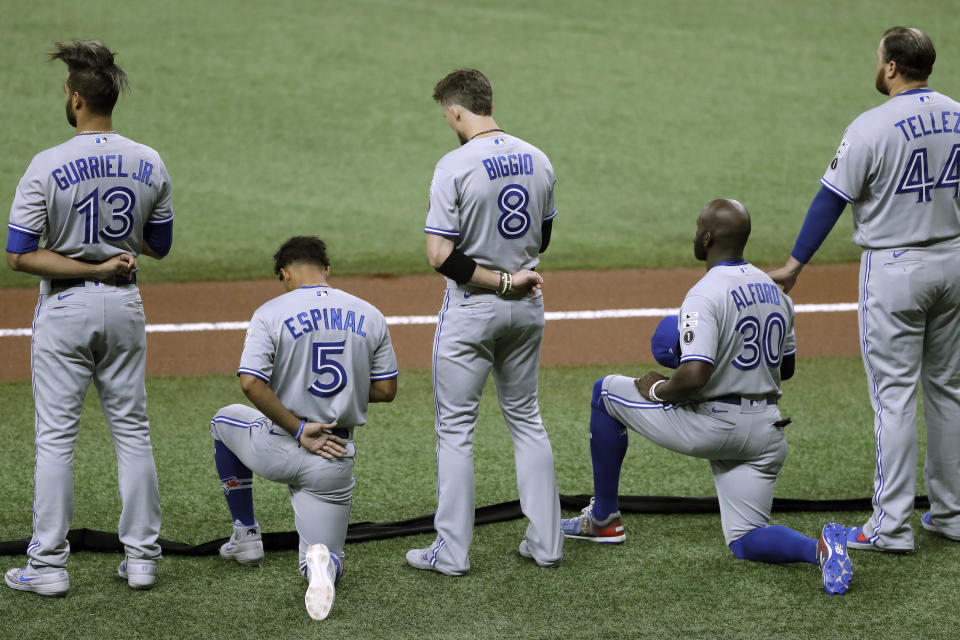 Lourdes Gurriel Jr., Cavan Biggio and Rowdy Tellez stand while Santiago Espinal and Anthony Alford kneel on the field during the U.S. national anthem.