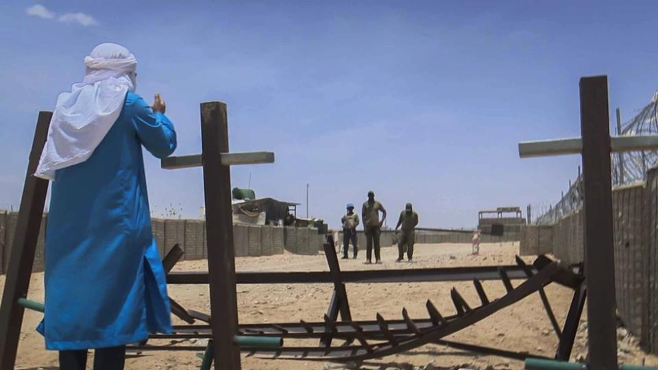 Feras stands at the gate of a UN base speaking to some people inside