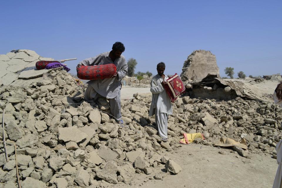 Survivors of earthquake collect their belongings near rubble of mud house after it collapsed following the quake in the town of Awaran