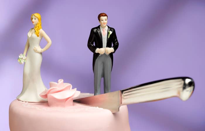 knife in the middle of a wedding cake with a bride figurine on one side of the blade and the groom on the other