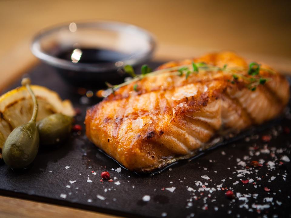 cooked salmon next to lemon and a brown sauce on a black tray