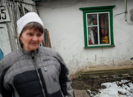 Pensioner Nadiya Ignatiy, 60, stands near her house as her grandson looks through the window in the village of Skryhalivka, Kiev region, Ukraine February 11, 2019. REUTERS/Gleb Garanich