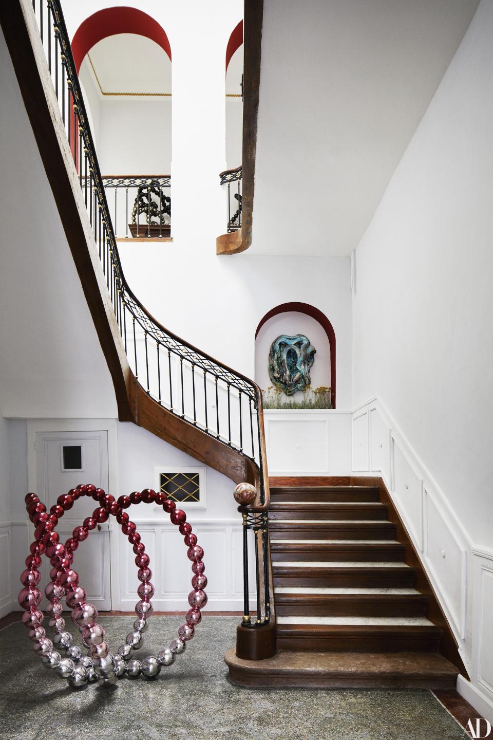 A glass–and–stainless steel sculpture by Othoniel stands at the foot of the stairway; glazed stoneware sculpture by Creten in arched niche.