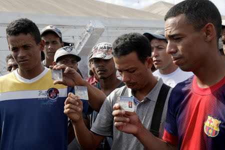 Members of Venezuela's National Guard Jean Carlos Cesar Parra, Carlos Eduardo Zapata and Jorge Luis Gonzalez Romero who defected to Brazil show their military IDs as they speak to the media near the border in Pacaraima, Brazil February 24, 2019. REUTERS/Ricardo Moraes