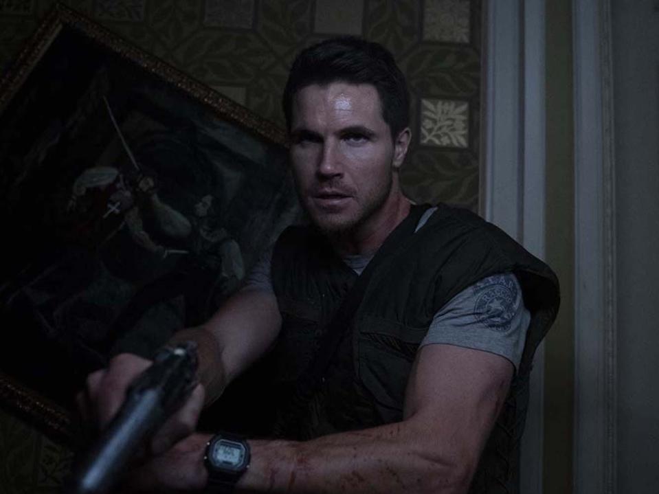 Robbie Amell as Chris Redfield holding a gun.