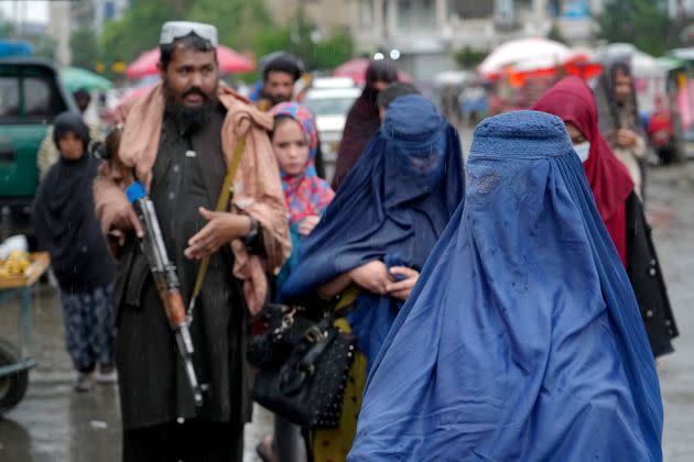 Covered women walk through a market as a Taliban fighter stands guard in the city of Kabul. (Photo: via Associated Press)