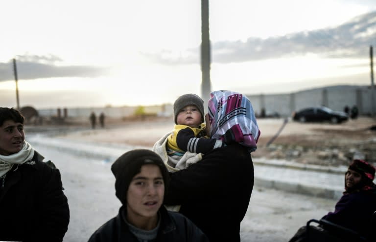 A woman holds a baby as they wait in Bab-Al Salama, next to the city of Azaz, northern Syria on February 5, 2016