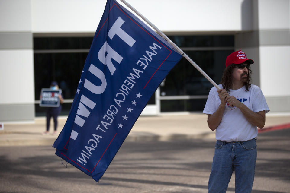 A Trump supporter holds up a flag as a Biden supporter holds up a sign outside of the Living Word Bible Church voting station in Phoenix, Ariz., on Election Day Tuesday, Nov. 3, 2020. (AP Photo/Dario Lopez-MIlls)