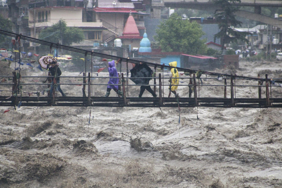 FILE - People walk through a bridge across River Beas swollen due to heavy rains in Kullu District, Himachal Pradesh, India, July 10, 2023. Scientists say increasingly frequent and intense storms could unleash more rainfall in the future as the atmosphere warms and holds more moisture. (AP Photo/Aqil Khan, File)