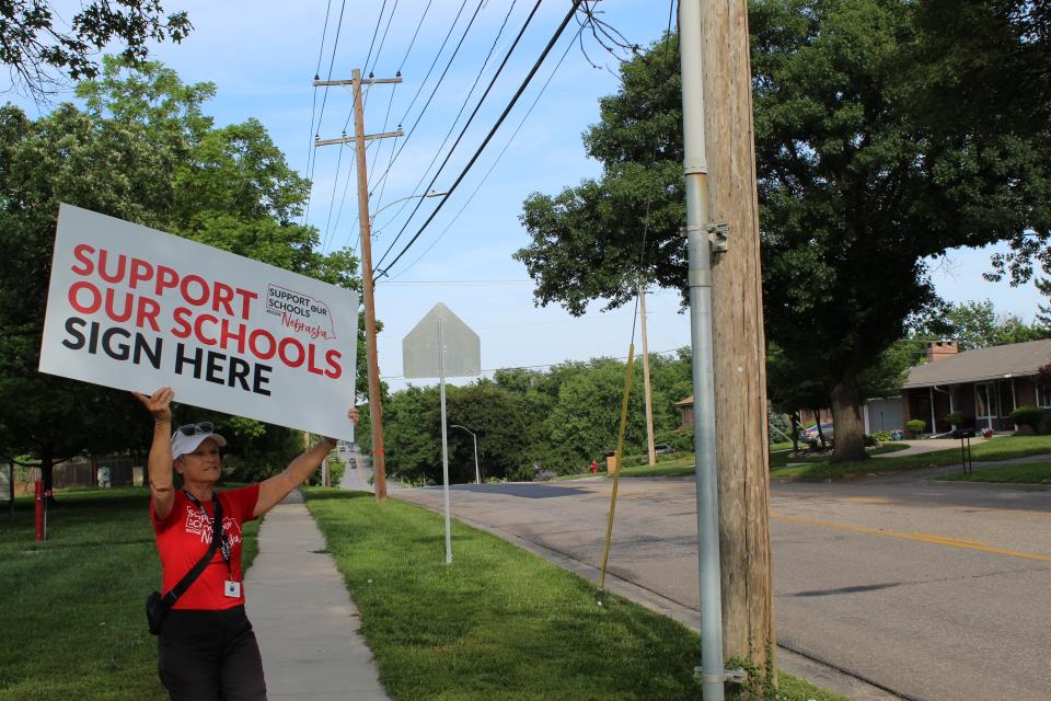 Deb Dulgar holds up a sign on a busy road in Lincoln, urging passing cars to stop and sign the Support Our Schools' petition. The group has until July 17th to collect enough signatures to get an initiative on the ballot for a second time.