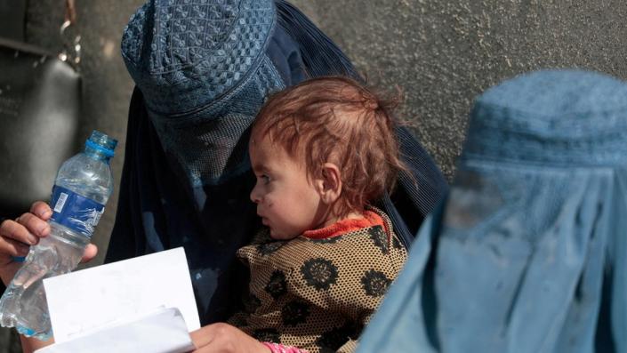 A displaced Afghan woman holds her child as she waits with other women to receive aid supply outside an UNCHR distribution center on the outskirts of Kabul