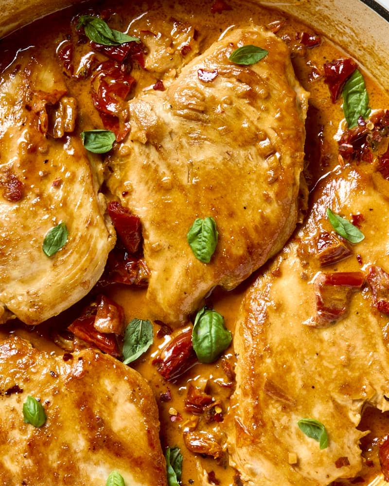 overhead shot of four pieces of marry me chicken in a red dutch oven.