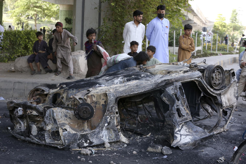 People look at a car burnt in Wednesday's clashes between police and the supporters of Pakistan's former Prime Minister Imran Khan, at a road, in Peshawar, Pakistan, Thursday, May 11, 2023. With former Prime Minister Imran Khan in custody, Pakistani authorities on Thursday cracked down on his supporters, arresting hundreds in overnight raids and sending troops across the country to rein in the wave of violence that followed his arrest. (AP Photo/Muhammad Sajjad)