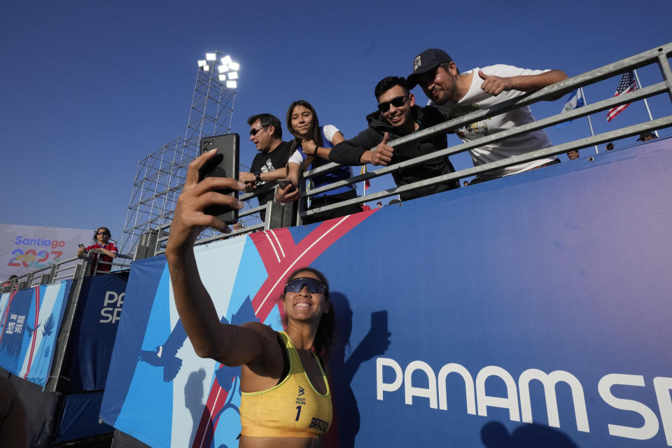 La brasileña Ana Silva se saca una selfie con espectadores tras la victoria ante la pareja de Estados Unidos en las semifinales del voleibol de playa femenino de los Juegos Panamericanos en Santiago, Chile, el jueves 26 de octubre de 2023. (AP Foto/Esteban Félix)