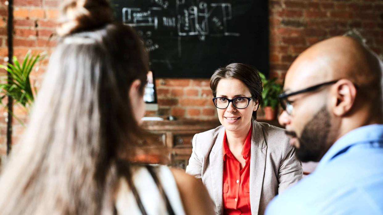 Over shoulder view of pretty middle-aged manager in eyeglasses chatting animatedly with colleagues while gathered together at modern office lobby.