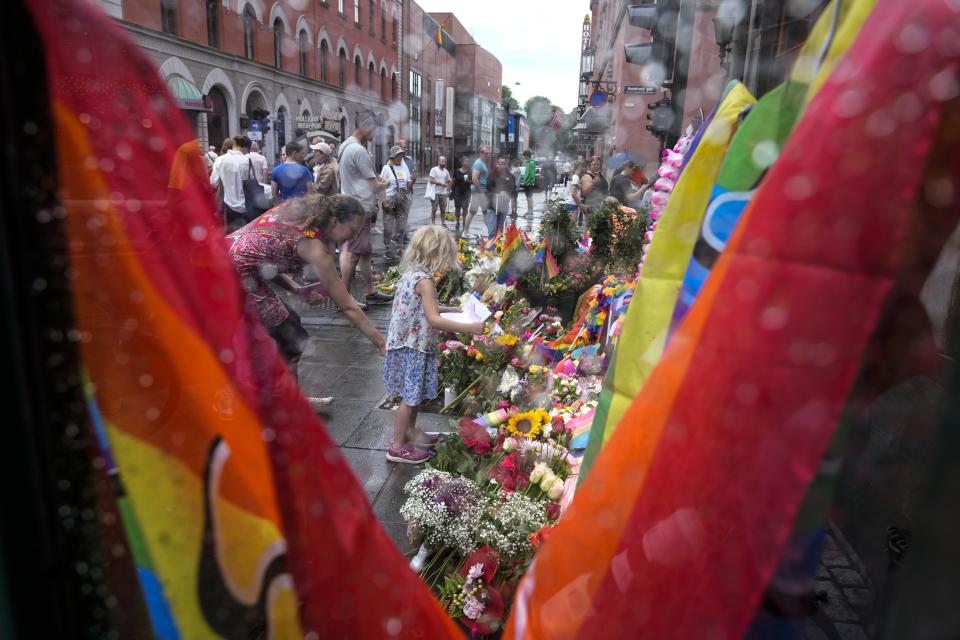 People lay flowers under the rain at the scene of a shooting in central of Oslo, Norway, Sunday, June 26, 2022. Norwegian police say they are investigating an overnight shooting in Oslo that killed two people and injured more than a dozen as a case of possible terrorism. In a news conference Saturday, police officials said the man arrested after the shooting was a Norwegian citizen of Iranian origin who was previously known to police but not for major crimes. (AP Photo/Sergei Grits)