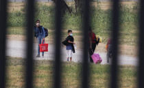 Migrants pass a fence near the International bridge where thousands of Haitian migrants have created a makeshift camp, Saturday, Sept. 18, 2021, in Del Rio, Texas. (AP Photo/Eric Gay)