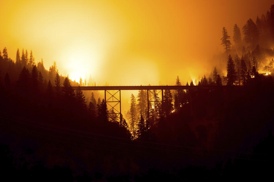 Seen in a long exposure photograph, the Dixie Fire burns behind a bridge in Plumas County, Calif., on Sunday, July 25, 2021. (AP Photo/Noah Berger)