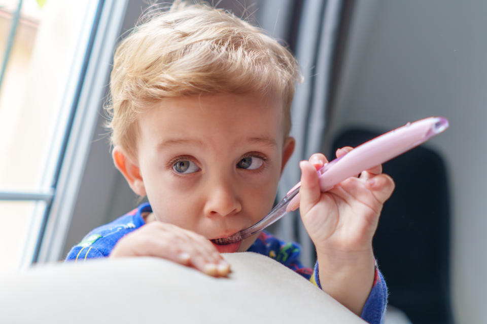 A young child is looking to the side while holding a toothbrush in their mouth