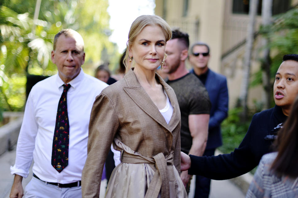 Nicole Kidman smiles at the camera wearing a brown trench coat