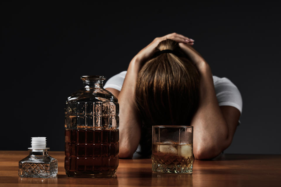 Young woman with hands on head while drinking whiskey alone in a bar.