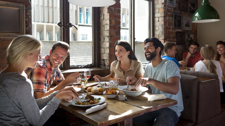 A group of four friends laugh and smile at one another as they enjoy a meal together in a restaurant