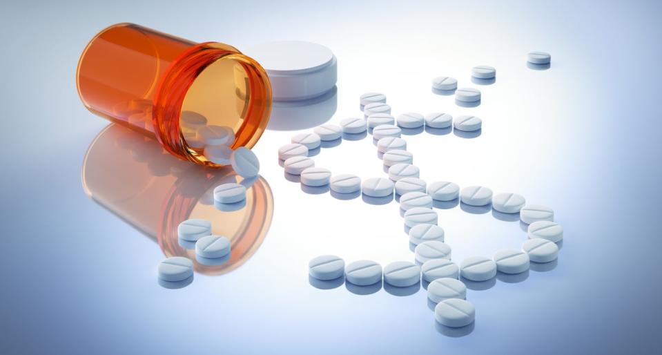 Numerous pills arranged into a dollar sign on a surface next to a pill bottle.