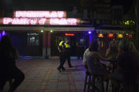 Police officers wearing face masks patrol as people sit on a terrace in Fuengirola, near Malaga, Spain, Saturday, Aug. 8, 2020. The increase in Spain of coronavirus outbreaks associated with nightlife has set off alarms in recent days, mainly in tourist areas where pubs and discos are full before the summer tourist campaign. (AP Photo/Jesus Merida)