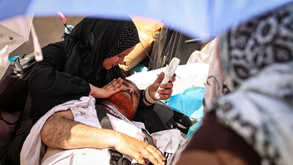 A woman uses a hand held battery run fan to cool off a man lying on the ground during the symbolic 'stoning of the devil' ritual at the annual hajj pilgrimage in Mina on June 16, 2024. - Fadel Senna/AFP/Getty Images