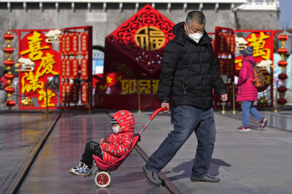 A man pulls a child past a Lunar New Year decoration on display at the Qianmen pedestrian shopping street, a popular tourist spot in Beijing, Tuesday, Jan. 17, 2023. China has announced its first population decline in decades as what has been the world's most populous nation ages and its birthrate plunges. (AP Photo/Andy Wong)