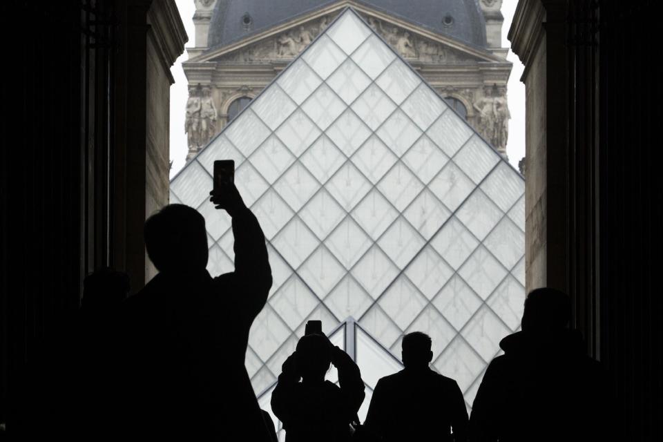 Tourists are silhouetted as they take pictures in the famed courtyard of the Louvre museum in Paris, Saturday, Feb. 4, 2017. The Louvre in Paris reopened to the public Saturday morning, less than 24-hours after a machete-wielding assailant shouting "Allahu Akbar!" was shot by soldiers, in what officials described as a suspected terror attack. (AP Photo/Kamil Zihnioglu)