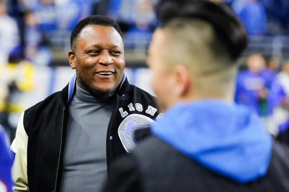 Barry Sanders, wearing a Lions jacket, chats on the field.