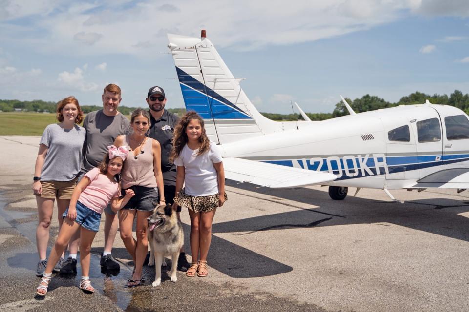 stolen dog returns home after four years poses with his family in front of a small plane