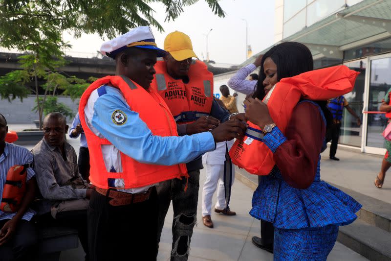 A Lagos State Ferry Service (LAGFERRY) official assists a passenger in wearing a life jacket at the Five Cowries Terminal in Falomo Lagos