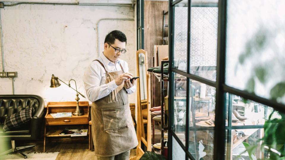 Smll business owner sending voice message while standing by window.