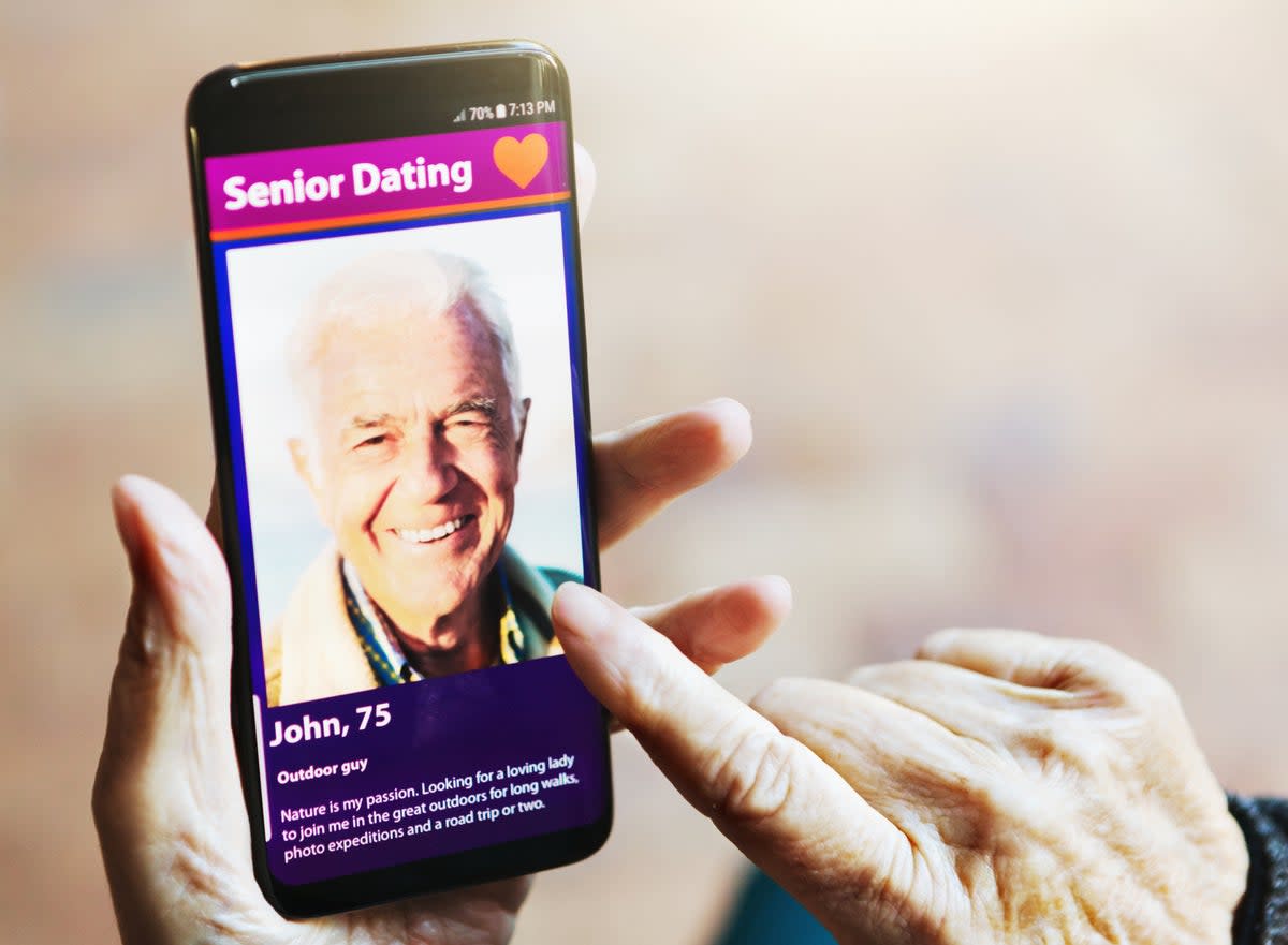 A senior woman's hand taps the screen of her phone, which shows a handsome senior man displayed on a dating app (Getty Images)