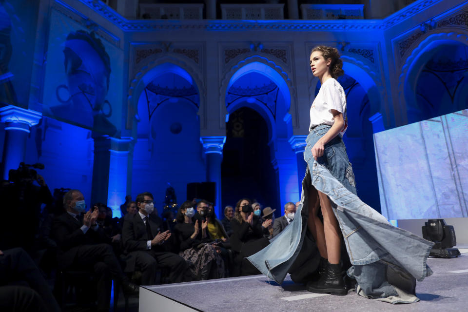 A model takes to the catwalk inside the 19th century building City Hall in Sarajevo, Bosnia, Thursday, Dec. 16, 2021, during the presentation of a collection dubbed "No Nation Fashion", a migrant-made fashion brand project. At the fashion show migrant models came out on the catwalks in designs meant to symbolize various stages of their journeys _ the 'nomadic' road away from home and the transit to new lives in new countries while the panel in the background read "We are strong," and "We smile." (AP Photo)