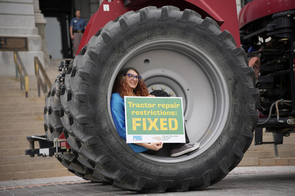 Colorado Rep. Brianna Titone sits in the wheel of a teactor on display before Colorado Gov. Jared Polis signed legislation that forces manufacturers to provide the necessary manuals, tools, parts and even software to farmers so they can fix their own machines Tuesday, April 25, 2023, during a ceremony outside the State Capitol in downtown Denver. Colorado is the first state to put the right-to-repair law into effect while at least 10 other states are considering similar measures. (AP Photo/David Zalubowski)