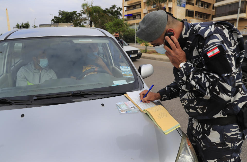 A Lebanese policeman writes a ticket for a car that violated the odd or even number plates car bans, as the country began a two-week lockdown to limit the spread of coronavirus that killed dozens of people over the past days, in Beirut, Lebanon, Saturday, Nov. 14, 2020. The lockdown comes after the number cases increased sharply in recent weeks around Lebanon straining the country's medical sector where intensive care units are almost full. (AP Photo/Hussein Malla)