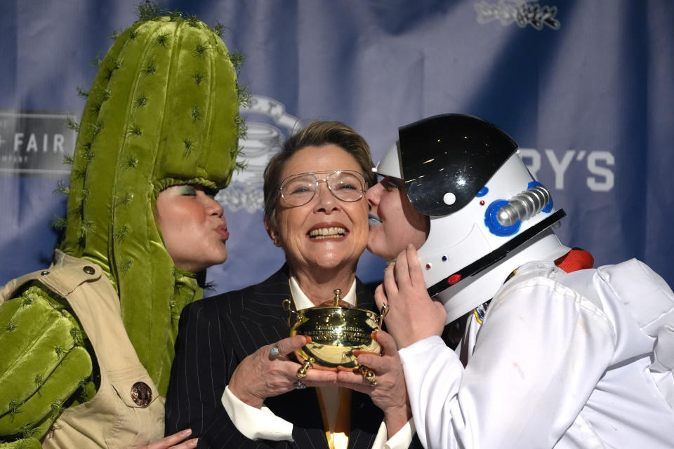 Actor Annette Bening, center, Hasty Pudding 2024 Woman of the Year, receives kisses from Harvard University theatrical students while holding the Pudding Pot during a news conference at Fargas Hall theater, Tuesday, Feb. 6, 2024, in Cambridge, Mass. The award was presented to Bening by Hasty Pudding Theatricals, a theatrical student society at Harvard University. (AP Photo/Steven Senne)