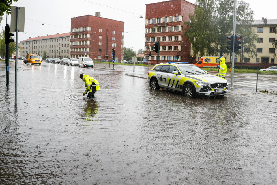 A police car is parked as an officer tries to open drains in a flooded street in Oslo following a heavy storm, Monday, Aug. 7, 2023. Stormy weather across the Baltic Sea region Monday caused airport delays, suspended ferry service, minor power outages and lots of rain. (Frederik Ringnes/NTB Scanpix via AP)