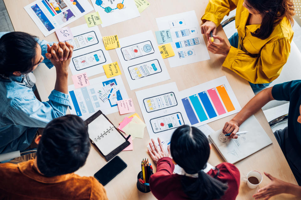 top view asian ux developer and ui designer brainstorming about mobile app interface wireframe design on table with customer brief and color code at modern office.Creative digital development agency