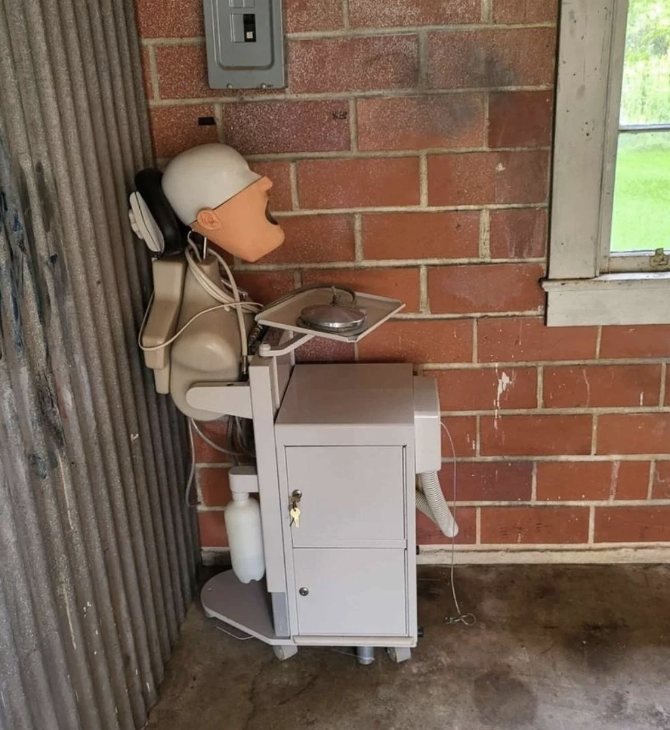 Mannequin head wearing large headphones attached to dental equipment, placed against a brick wall in a rustic setting