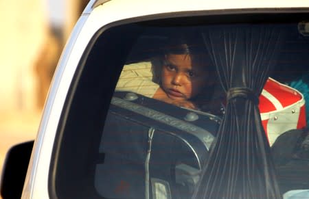 A child is seen in a vehicle with belongings as they flee, in Tel Abyad