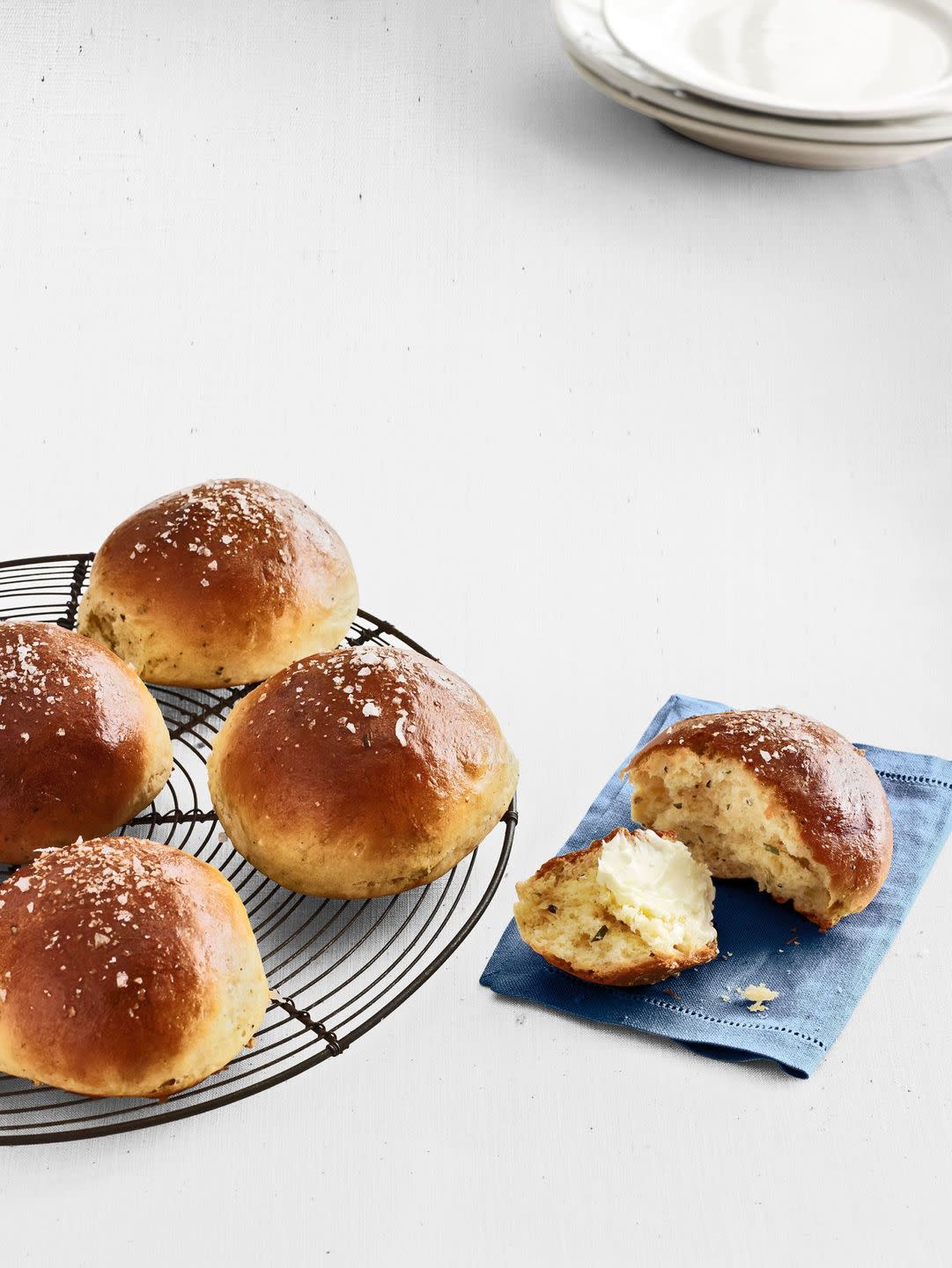 rosemary brioche rolls on a wire rack and one torn open on a blue linen napkin with butter