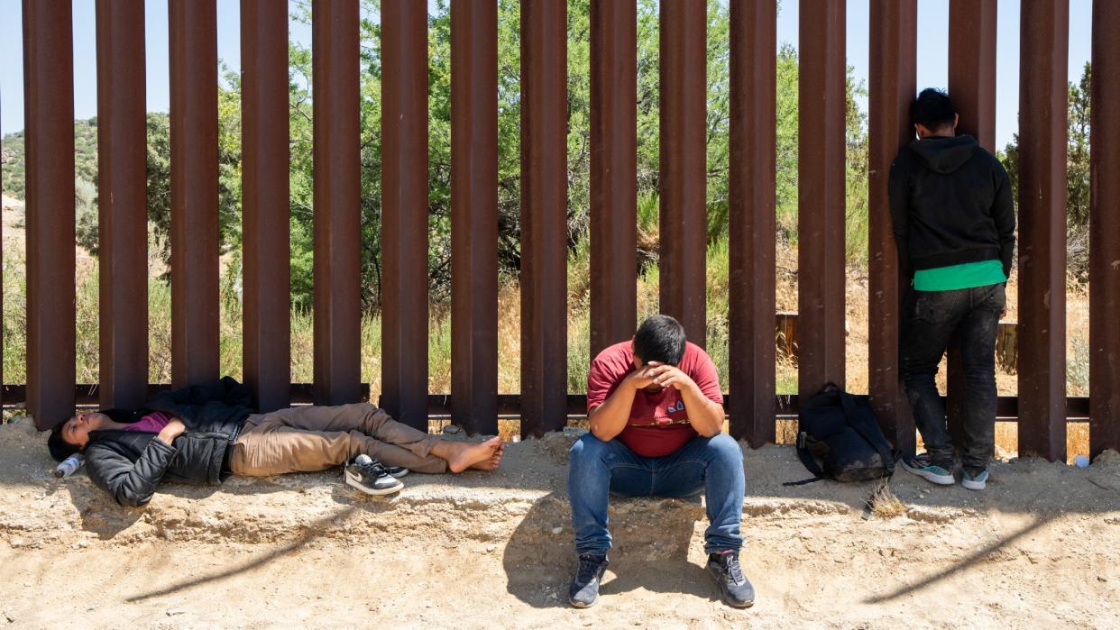  Migrants rest at the iron border fence as they wait to be processed by the US Border Patrol agents near Jacumba Hot Springs, California. 