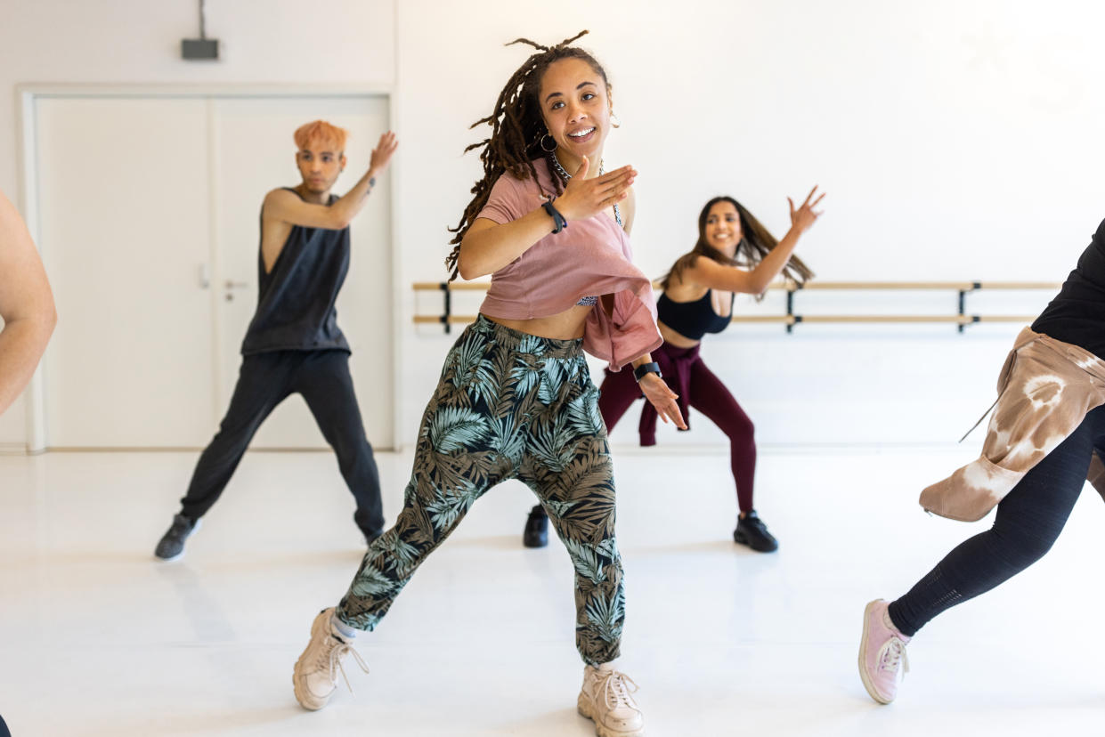 Confident young woman practicing dance moves at fitness club gut health. Group of people doing fitness dance in a class.